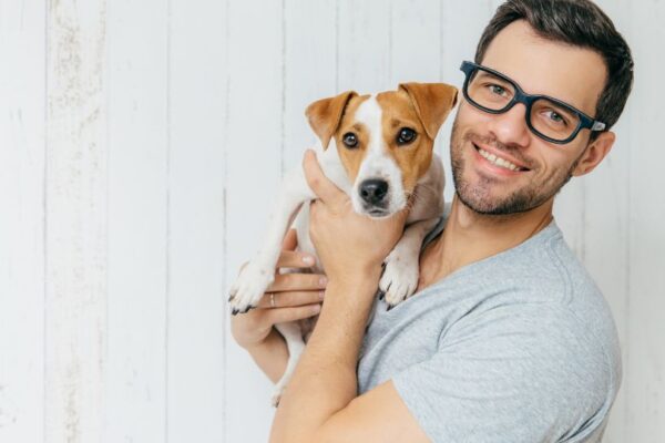 Un uomo sorride mentre tiene in braccio un cucciolo di cane con orecchie marroni.