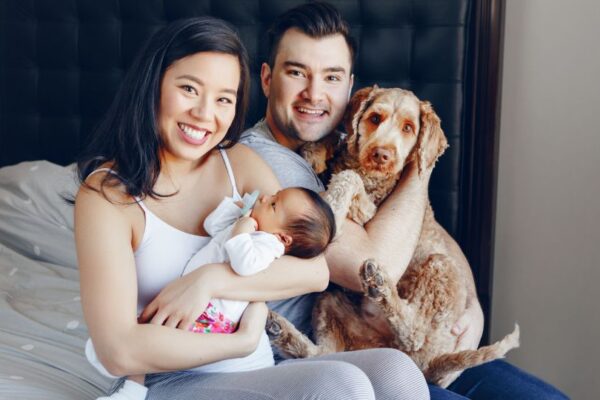 Una famiglia felice con un neonato e un cane, sorridendo insieme sul letto.