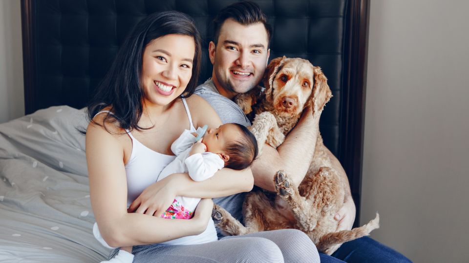 Una famiglia felice con un neonato e un cane, sorridendo insieme sul letto.