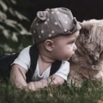 Un neonato sdraiato sull'erba accanto a un cane, entrambi curiosi.