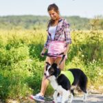 Una donna sorridente passeggia con un cane in un campo verde.